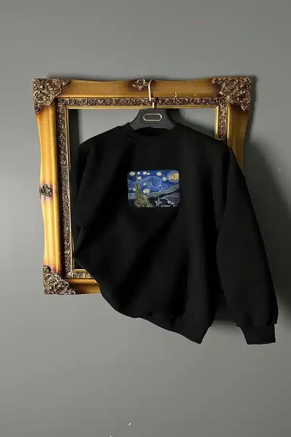 دورس مشکی اورسایز با طرح گلدوزی شده شب پرستاره ونگوگ از برند اوتانا که به شکلی هنری در یک قاب عکس طلایی آویزان شده است. دورس اورسایز گلدوزی طرح شب پرستاره ونگوگ